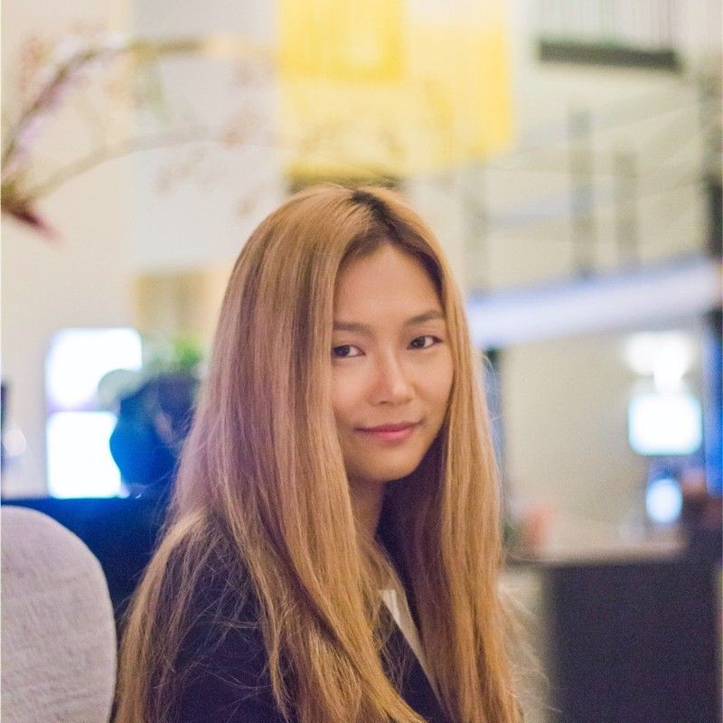 Person with long hair smiling in a blurred indoor setting.